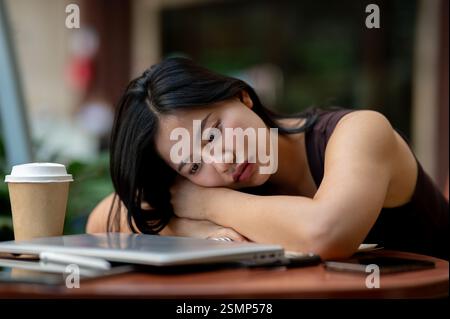 Une femme asiatique triste et fatiguée pose le visage sur la table à l'extérieur, se sentant épuisée du travail. surmené, problème de santé mentale, épuisé, stress Banque D'Images
