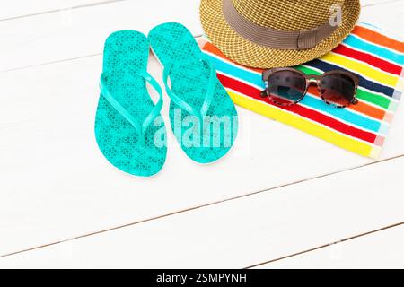 Tongs lumineuses, chapeau élégant et lunettes de soleil sur une serviette de plage colorée prête pour une journée au soleil Banque D'Images