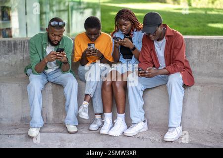Jeunes gars afro-américains collés à des smartphones, discutant et naviguant sur les médias sociaux dans le parc Banque D'Images