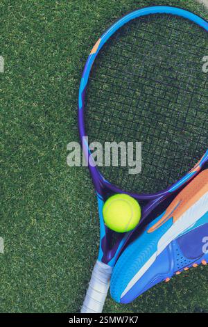 Raquette de tennis et balle jaune vif placée sur l'herbe verte avec des chaussures de sport à proximité pendant la séance d'entraînement de jour Banque D'Images