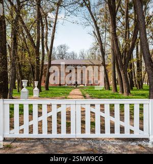 Clôture en bois blanc avec porte menant au palais Dunin-Vonsovich du XVIIIe siècle (1792) dans le parc. Le printemps à la campagne. Banque D'Images