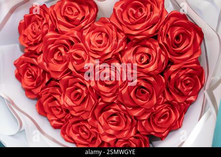 Un beau bouquet de roses rouges en forme de cœur, fabriqué à partir de tissu satiné, affiché sur un fond de couleur claire. Parfait pour offrir sur occ romantique Banque D'Images