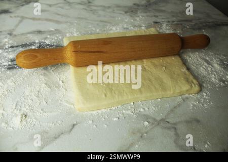 Le rouleau à pâtisserie repose sur une couche de pâte à levure feuilletée. Gâteaux faits maison. Banque D'Images