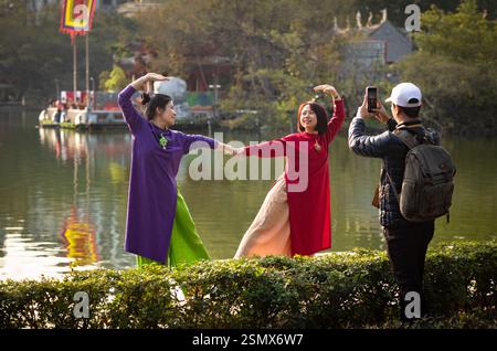 Deux femmes vietnamiennes habillées en traditionnel ao dai se tiennent la main et forment la forme d'un cœur pour poser pour des photographies du lac Hoan Kiem, Hanoi, Vietnam Banque D'Images