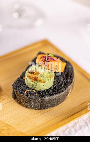 Canapés de pain noir gourmet surmontés de tartinades colorées, de microgreens et de garnitures croquantes, servis sur une planche de bois élégante Banque D'Images