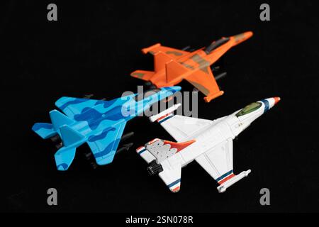 Ensemble de trois jets de chasse jouet en bleu, orange et blanc sur fond noir. Concept de modèles d'avions militaires. Banque D'Images