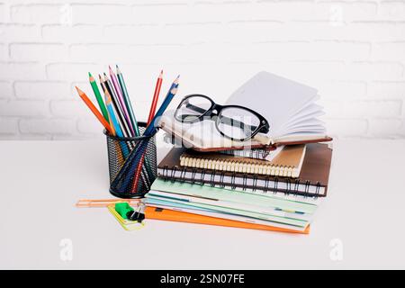 Articles de papeterie colorés et lunettes disposés sur un bureau avec des blocs-notes prêts pour l'étude ou le travail créatif dans un environnement lumineux Banque D'Images