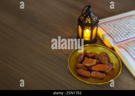 Un bol de dattes, une lanterne allumée et un Al Coran ouvert sur une table en bois, symbolisant le mois sacré islamique du Ramadan. Copier l'espace pour le texte. Banque D'Images