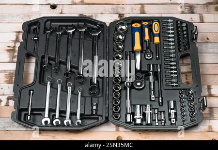 Trousse à outils complète avec diverses clés et douilles organisées dans un boîtier noir sur une surface en bois Banque D'Images
