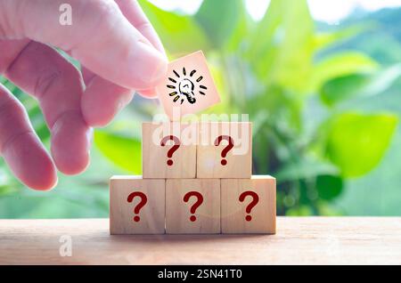 Main mettant cube en bois avec ampoule sur le dessus de l'autre symbole de point d'interrogation. Concept d'idée commerciale Banque D'Images
