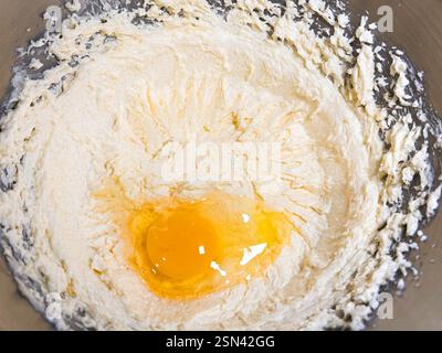 Battre le beurre, le sucre et les œufs dans un bol en métal gris. Le processus de fabrication de gâteaux et de biscuits en mélangeant du beurre, des œufs et du sucre. Gros plan d'un œuf en cr Banque D'Images