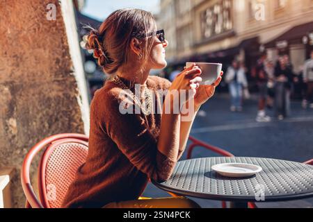 Jeune femme élégante est assise sur la terrasse du café en plein air buvant du café. Femme aime l'architecture de la ville européenne sur la rue Banque D'Images