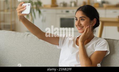 Indienne femme souriante influenceur vlogger blogueur Arabian Girl femme faire selfie photo avec téléphone portable posant canapé assis canapé à la maison smartphone Banque D'Images