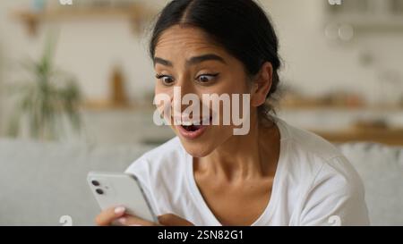Joyeux sourire excité joyeux étonné surpris Wonder femme hindoue fille indienne femme arabe à la maison lecture étonnante bonne nouvelle en ligne offre internet Banque D'Images