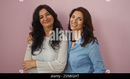 Deux femmes d'âge moyen, peut-être sœurs ou amies, souriant chaleureusement ensemble sur un fond rose isolé, incarnant l'amour, la famille et les compagnons Banque D'Images