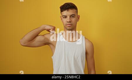 Jeune homme avec une pose musclée se tient confiant sur un fond jaune vif, portant un débardeur blanc, mettant en valeur la force et le charisme dans un Banque D'Images