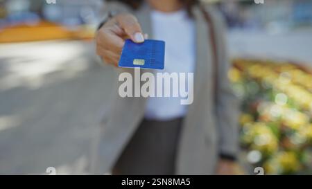 Femme offrant une carte de crédit à l'extérieur dans un parc urbain, mettant en valeur le concept financier avec l'accent sur le paiement et la transaction dans le cadre de la ville, backgro flou Banque D'Images