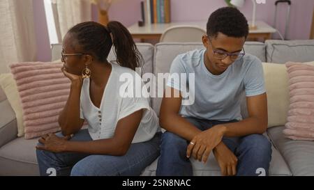 Mère et fils assis sur un canapé regardant vers le bas avec des expressions sérieuses dans un salon confortable, signifiant conflit familial ou contemplation Banque D'Images