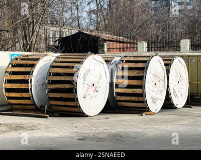 Lviv, Ukraine - 12 février 2025 : plusieurs grandes bobines en bois stockées à l'extérieur, entourées d'infrastructures industrielles et de nature. Banque D'Images