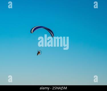 Pilote assis conduisant un parapente motorisé dans un ciel bleu clair Banque D'Images