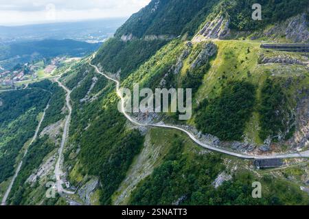Route de montagne sinueuse traversant des pentes vertes abruptes. La vue aérienne met en évidence le terrain isolé et difficile, idéal pour les voyages d'aventure et les voyages en voiture. Banque D'Images