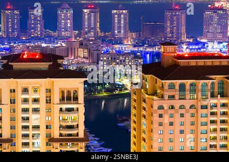 Vue nocturne à grand angle des bâtiments de luxe illuminés, des marinas et des magasins en bord de mer à Doha Pearl Island le long du golfe Persique à Doha, Qatar. Banque D'Images