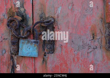 Une photo en gros plan d'une chaîne rouillée et d'un cadenas bleu délavé fixant une vieille porte en bois rouge. Banque D'Images