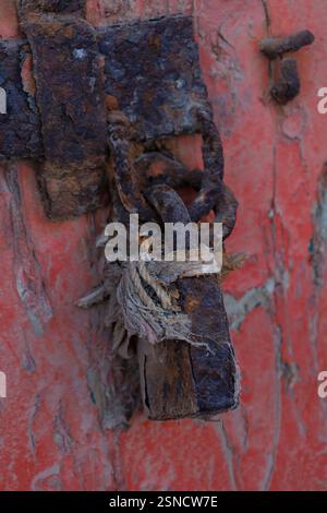 Une photo en gros plan d'une chaîne rouillée et d'un cadenas bleu délavé fixant une vieille porte en bois rouge. Banque D'Images