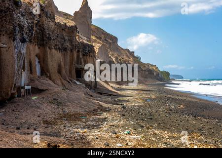 Un paysage côtier accidenté avec d'imposantes falaises érodées avec des formations rocheuses volcaniques sombres. Une petite grotte abandonnée à Santorin Banque D'Images