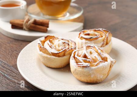Roses aux pommes fraîchement cuites, miel, bâtonnets de cannelle et thé sur une table en bois, gros plan Banque D'Images