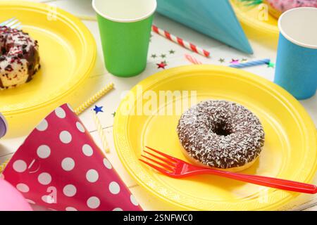 Assiettes en plastique avec des beignets savoureux et décor pour la fête d'anniversaire sur la table en bois clair, gros plan Banque D'Images
