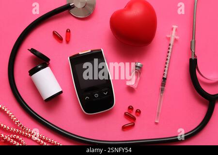 Glucomètre moderne avec ampoule d'insuline, seringue, stéthoscope, pilules et coeur sur fond rose Banque D'Images