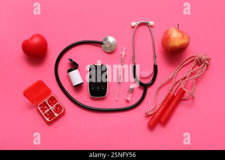 Glucomètre moderne avec ampoule d'insuline, seringue, stéthoscope, pilules et pomme sur fond rose Banque D'Images
