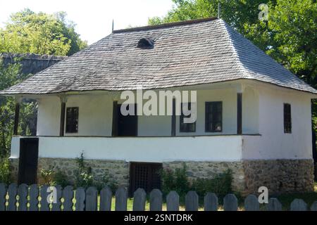 Musée du village, Bucarest, Roumanie. Maison en bois du XIXe siècle du comté d'Arges, avec toit en bardeaux en bois, balcon, fondation en pierre et cave. Banque D'Images