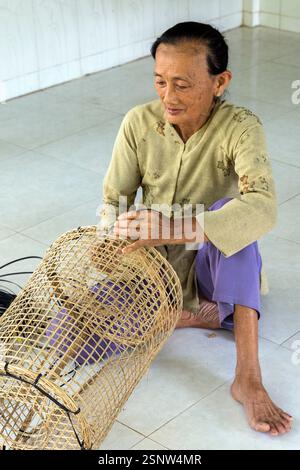 Une femme assise sur le sol d’un atelier rural fabriquant des pièges à poissons en bambou, Cho Lach, Vietnam, lundi 11 novembre, 2024. Banque D'Images