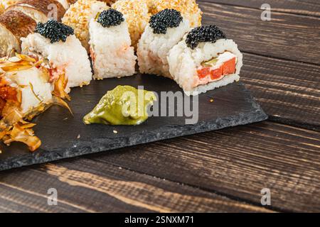Un élégant assortiment de sushis avec du crabe, du caviar et du wasabi présenté sur un tableau d'ardoise sombre. Rouleaux parfaitement conçus présentant des couleurs vives a Banque D'Images