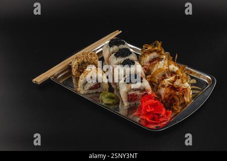 Un plateau magnifiquement arrangé de rouleaux de sushi se trouve sur un plateau métallique. Divers rouleaux sont recouverts de sésame, de caviar et accompagnés de gingembre mariné an Banque D'Images
