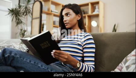 Femme, Bible et pensée avec la religion sur le canapé à la maison pour la lecture, la connaissance ou l'écriture pour le guide spirituel. Personne, fille et livre chrétien avec Banque D'Images
