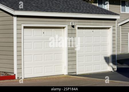 Vue rapprochée d'un garage double avec portes blanches lambrissées, murs extérieurs beiges et un petit luminaire extérieur monté entre les portes. Banque D'Images