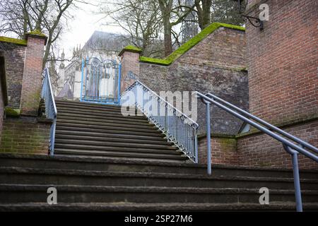 Escalier en pierre avec garde-corps en métal menant à une porte bleue ornée et des murs de briques recouverts de mousse, avec une cathédrale en arrière-plan à Amiens, France Banque D'Images