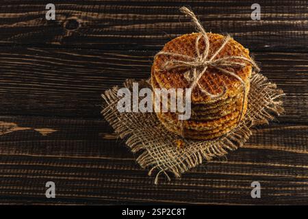 Une pile de gaufres au caramel fraîchement préparées nouées avec de la ficelle se trouve au sommet d'une toile de jute sur une table en bois rustique, mettant en vedette un délice pour célébrer Banque D'Images