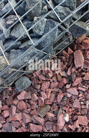 Toile de fond texturée de roches de granit clôturées dans le mur de gabion et pierres décoratives de gravier rouge pour les décorations extérieures. Pierres idées de décoration Banque D'Images
