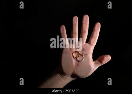 Une main montre deux bagues de mariage, une en or et une en argent, reposant dans la paume. Les anneaux brillent subtilement sur un fond sombre, symbolisant l'amour an Banque D'Images