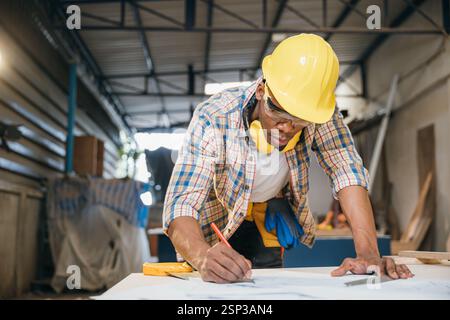 Menuisier dessinant des plans de table sur bois à un bureau de travail. constructeurs et ingénieurs concevant Banque D'Images