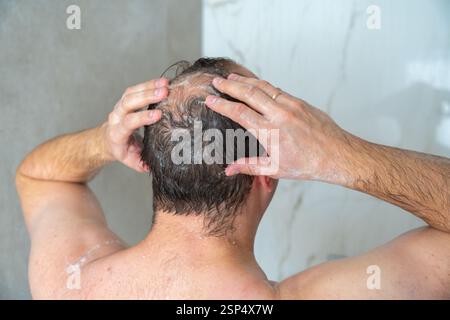 l'homme se baigne la tête dans la douche, la tête avec une tache chauve, debout dos à la caméra, gros plan. Vidéos 4K de haute qualité Banque D'Images