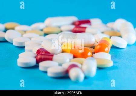 Différents types de pilules et de capsules sont dispersés sur un fond bleu vif, soulignant leurs formes et couleurs variées. Banque D'Images
