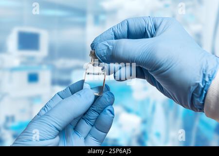 Un professionnel de la santé portant des gants bleus tient soigneusement un petit flacon transparent de liquide tout en se préparant à une intervention médicale dans un cadre clinique. Banque D'Images