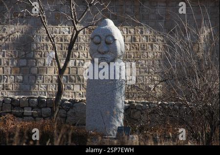 Dol Hareubang. Statue coréenne avec visage altéré et inscription, flanquée d'un panneau moderne avec flèches directionnelles et texte coréen. Corée du Sud. Banque D'Images