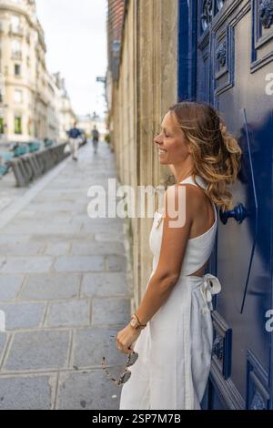 'Femme élégante en combinaison blanche, veste, rue Paris, porte bleue.' Banque D'Images