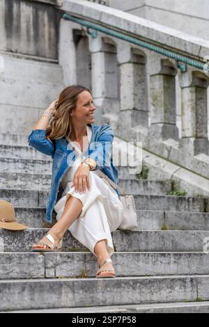 Femme assise sur des marches de pierre à Paris portant une veste en denim Banque D'Images